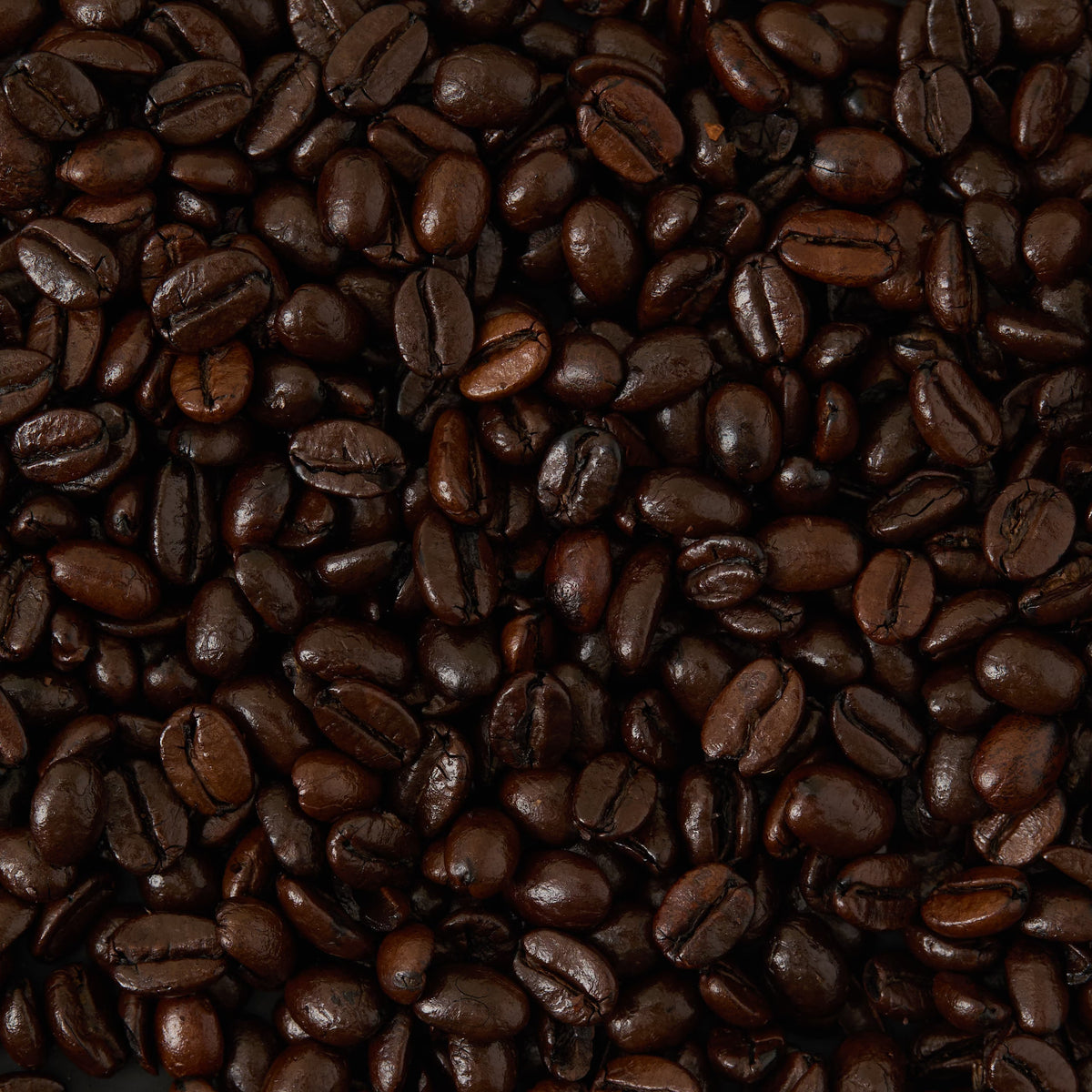 A close-up of many shiny Monsoon Malabar Coffee Beans Valve Pack dark roasted coffee beans tightly packed together, filling the entire frame.