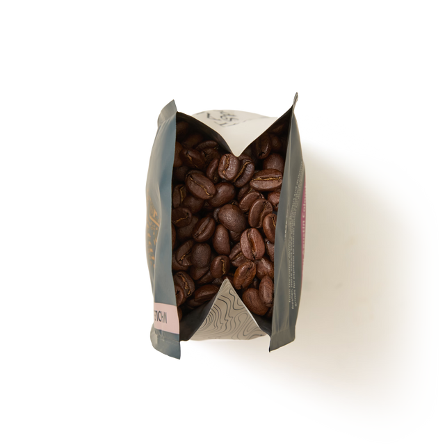 A top-down view of an open San Agustin Colombia Coffee Beans Valve Pack filled with roasted coffee beans, with the bag’s sides folded outward, on a plain white background.