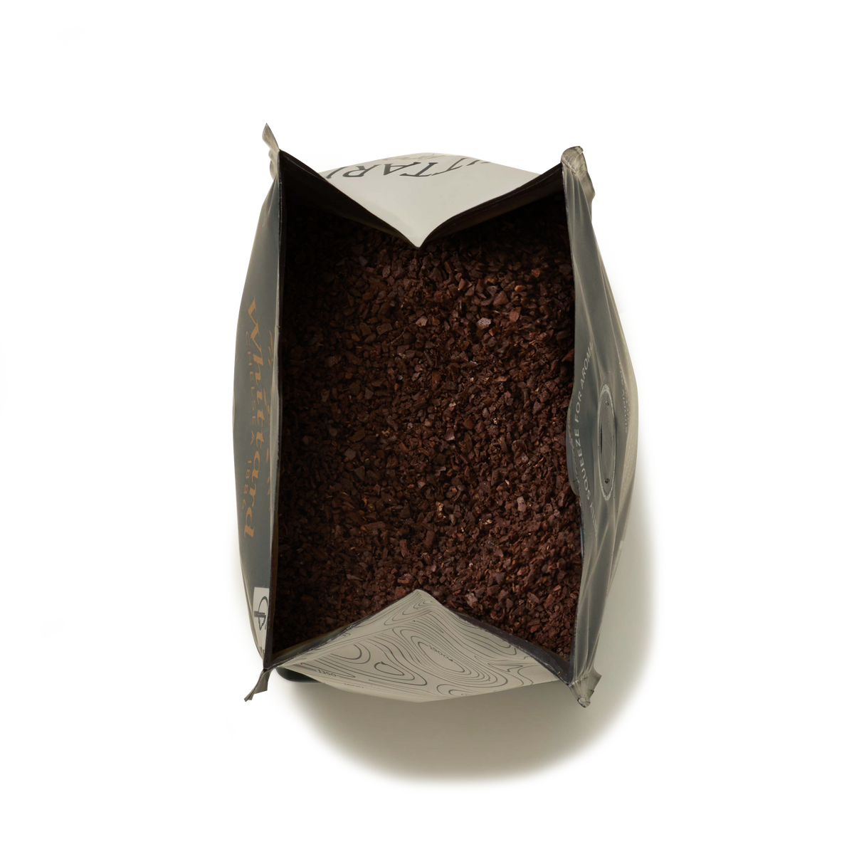 A top-down view of an open Whittard House Blend Ground Coffee Valve Pack reveals a generous amount of dark brown Colombian coffee grounds inside, set against a white background.