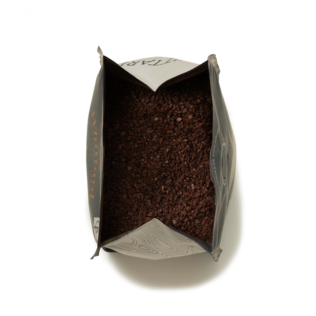 A top-down view of an open Whittard House Blend Ground Coffee Valve Pack reveals a generous amount of dark brown Colombian coffee grounds inside, set against a white background.
