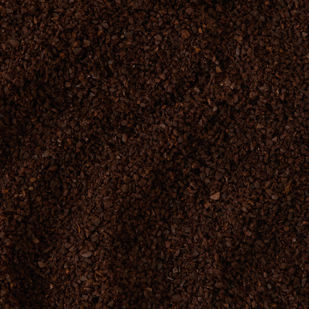 A close-up view of a pile of Santos and Java Ground Coffee Valve Pack, highlighting its dark brown color, coarse texture, and uneven granules.
