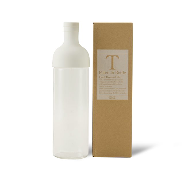 A clear bottle with a white cap stands next to a brown box labeled Filter-in Bottle Cold Brewed Tea on a white background.