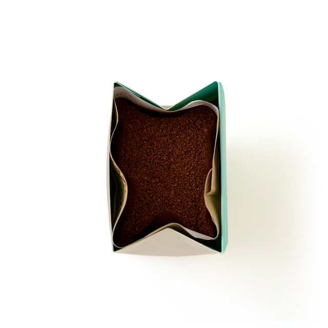 Open top view of a green paper bag filled with brown granular Amaretto Flavoured Ground Coffee against a white background.