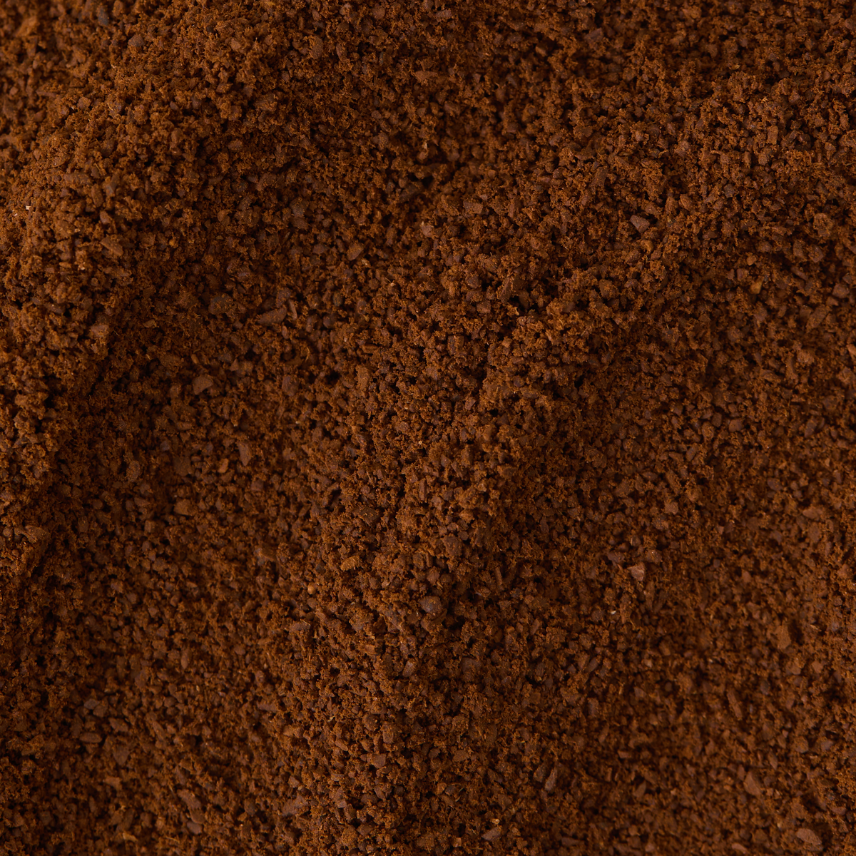 A close-up of a pile of Chocolate Brownie Flavoured Ground Coffee showcases its finely ground texture, with small ridges and an uneven surface adding depth and visual interest.