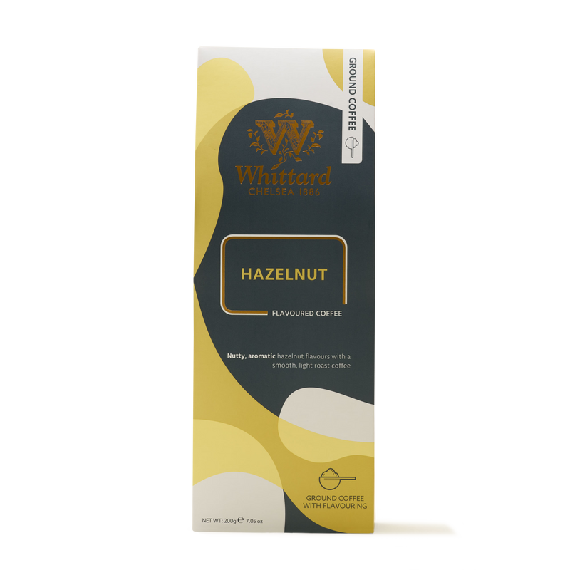 A box of Hazelnut Flavoured Ground Coffee featuring an elegant gold, cream, and dark green design. The packaging highlights its nutty, aromatic hazelnut taste inspired by the classic French café noisette and notes that it is omni-grind coffee with flavoring—ideal for savoring as your everyday brew.
