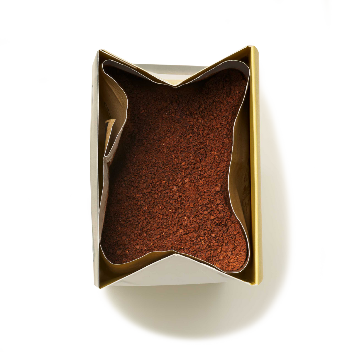 An open rectangular container filled with finely ground Hazelnut Flavoured Ground Coffee, viewed from above, with the paper liner folded back to reveal the coffee inside.