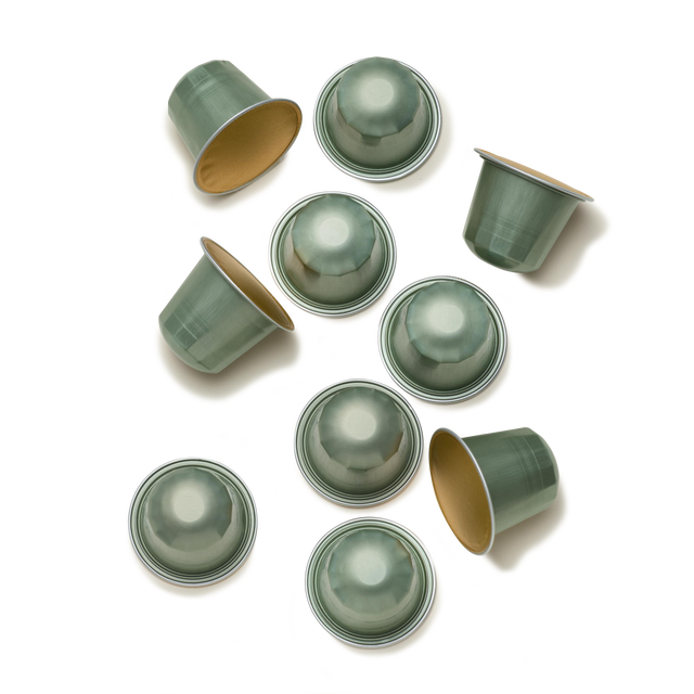 Nine green Guatemala Elephant Nespresso Compatible Coffee Pods are scattered on a white background, with some capsules facing up to reveal their flat tops and others upside down, exposing the golden interiors—each pod reflecting the rich flavors of coffee made from large beans grown near Lake Atitlán.