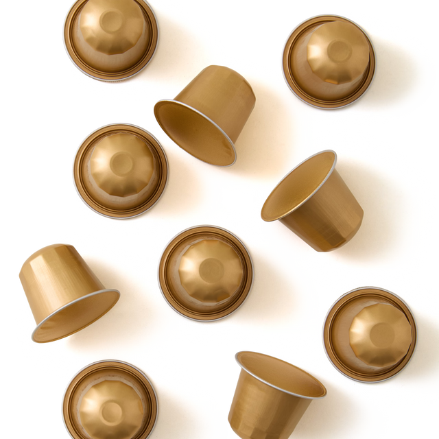 Nine gold-colored coffee pods are arranged randomly on a white background, some facing upward and others sideways or upside down.