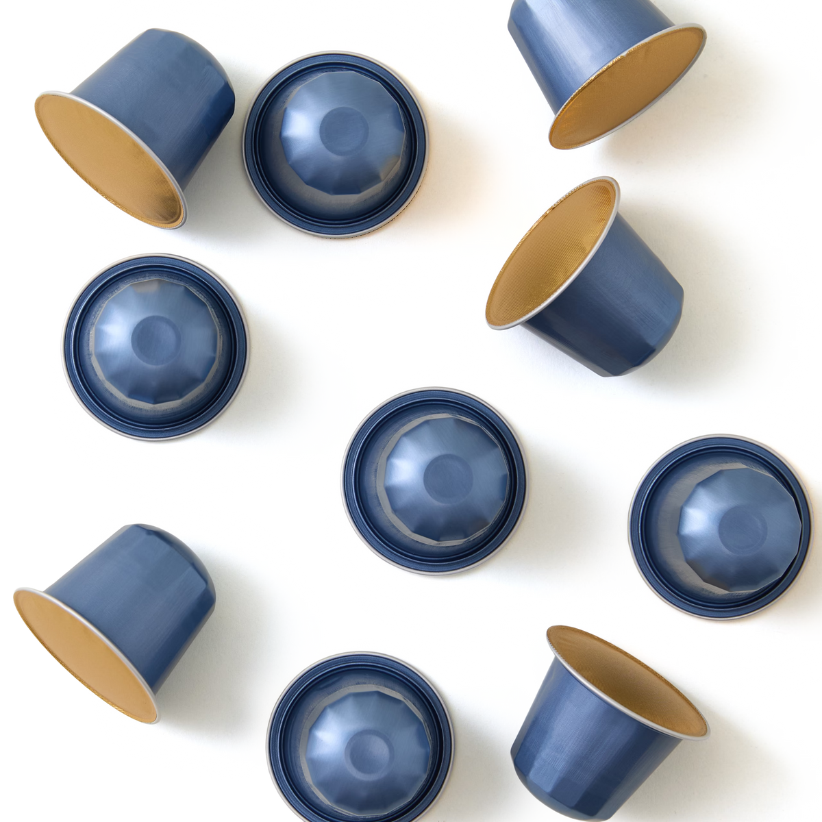Nine blue coffee capsules with gold interiors are arranged in a scattered pattern on a white background, with some capsules facing up and others facing down.