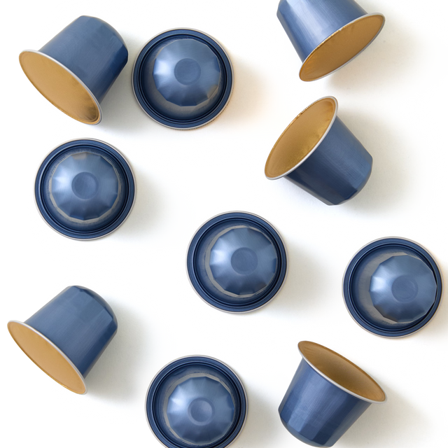 Nine blue coffee capsules with gold interiors are arranged in a scattered pattern on a white background, with some capsules facing up and others facing down.