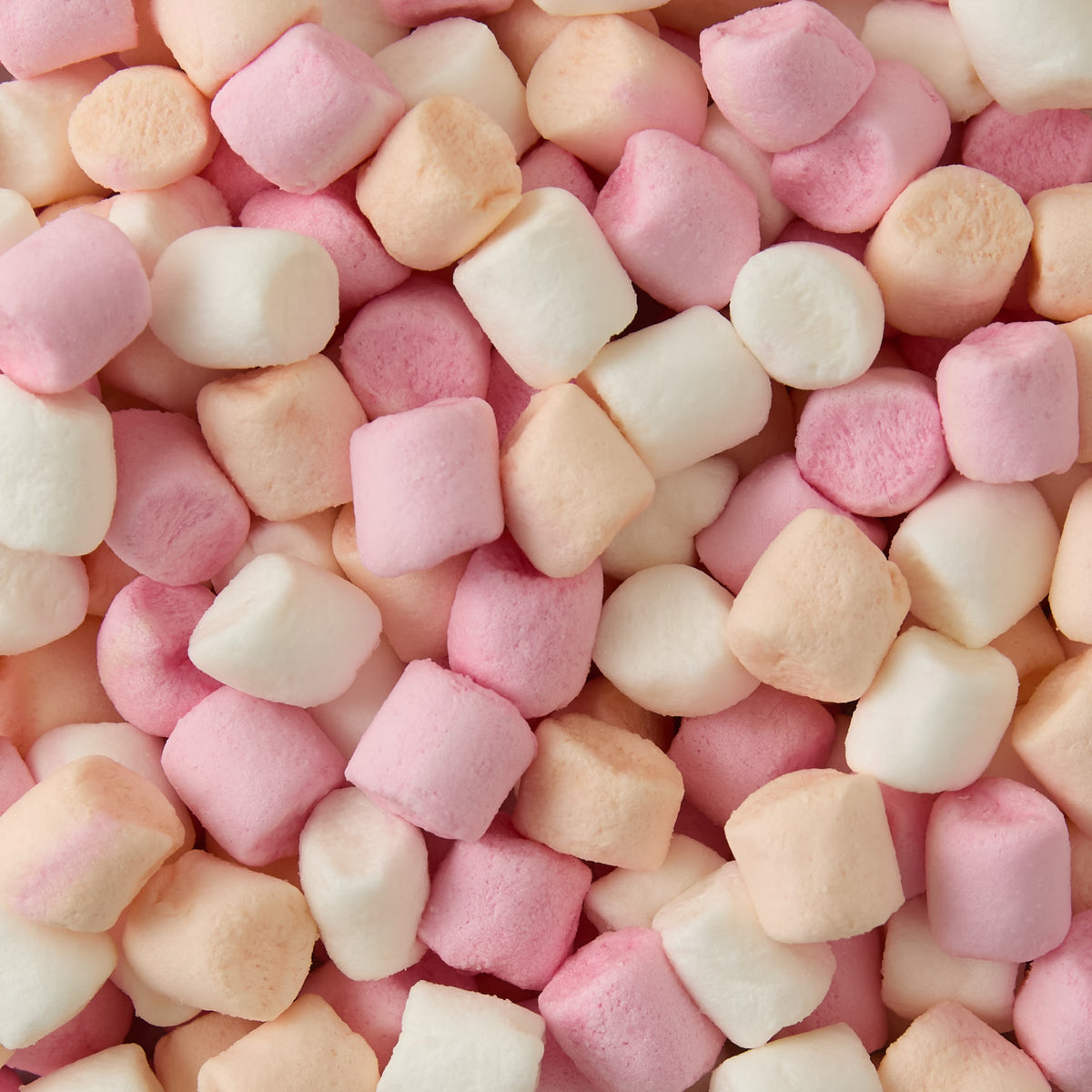 A close-up view of pastel-colored mini marshmallows in white, pink, and light peach shades, scattered and piled together.