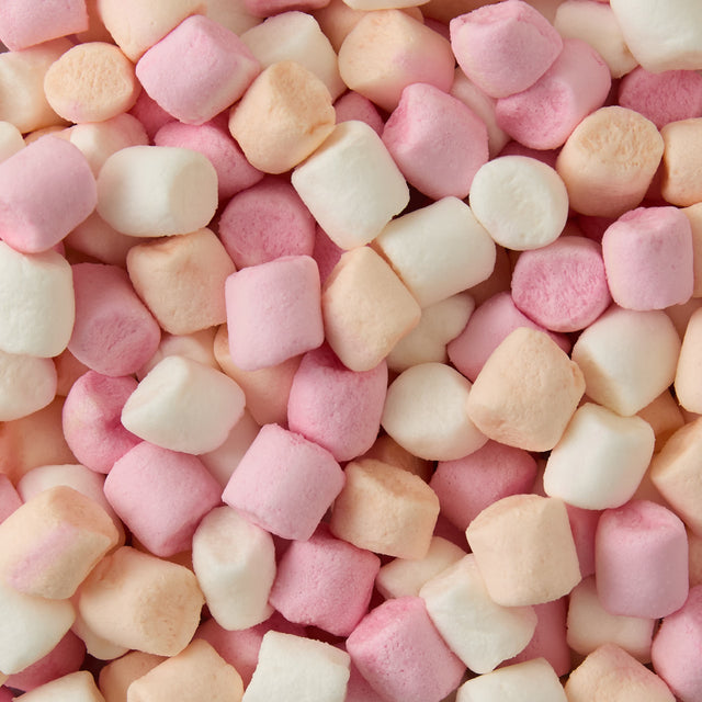A close-up view of pastel-colored mini marshmallows in white, pink, and light peach shades, scattered and piled together.