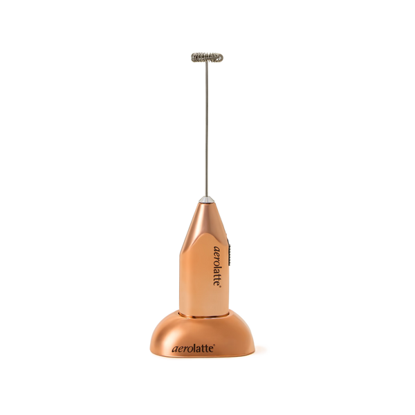 A metallic orange handheld Aerolatte milk frother with a matching stand, shown upright on a plain white background.