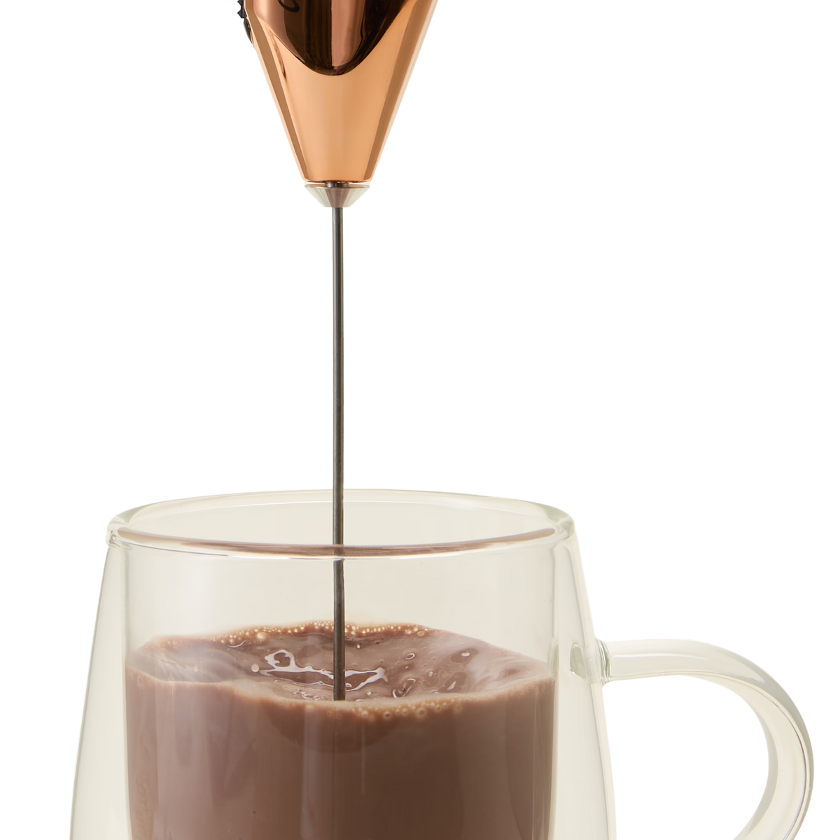 A handheld milk frother mixes chocolate milk in a clear glass mug, creating bubbles on the surface of the drink.