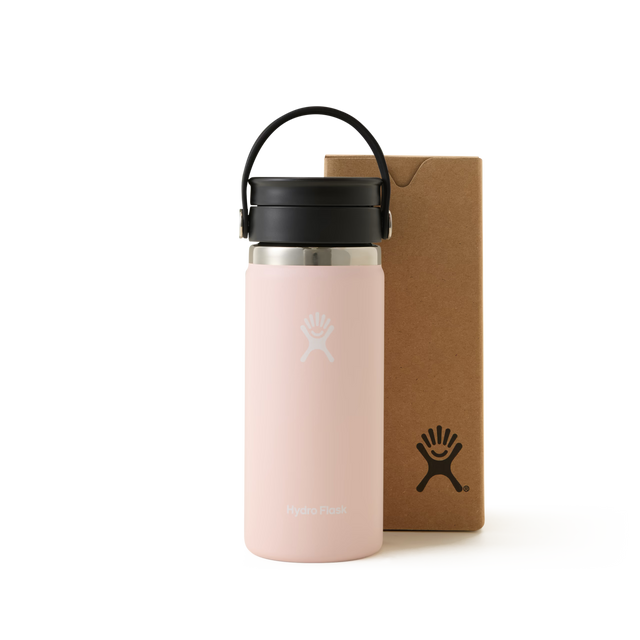A Trillium Hydro Flask Travel Mug in light pink, featuring a black lid and handle, is placed next to a brown box with the Hydro Flask logo, all set against a white background. This stylish Trillium travel mug is perfect for keeping your drinks at the ideal temperature while you’re on the go.