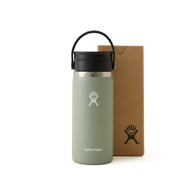 A light green Hydro Flask water bottle with a black lid and handle is standing next to a brown cardboard box, both featuring the Hydro Flask logo, against a white background.