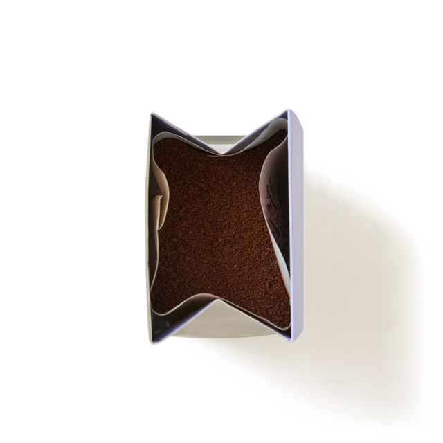 A top view of an open container filled with Vanilla Flavoured Ground Coffee, showing the brown coffee granules inside against a white background.