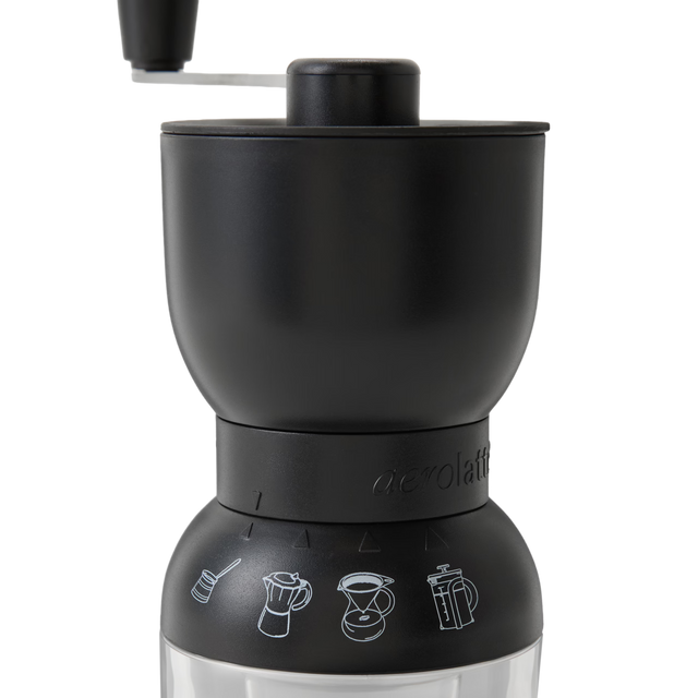 A black manual coffee grinder with a clear bottom and white icons showing different coffee brewing methods, including pour-over and French press, on the grinders middle section.