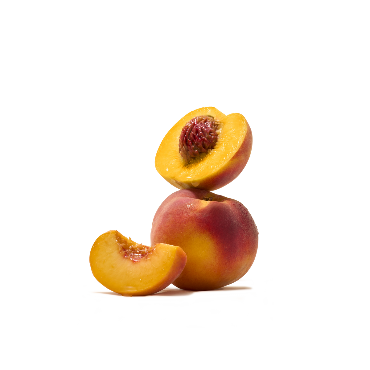 A whole peach rests on a white surface, topped with a halved peach and accompanied by a peach slice in front. The ripe fruit, showcasing yellow-orange flesh and reddish skin, captures the essence of Peach Flavour Instant Tea—ideal for crafting a deliciously refreshing beverage.