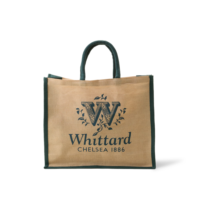 The Whittard Medium Jute Cotton Bag is a tan and green reusable shopping bag made from durable jute cotton, featuring “Whittard Chelsea 1886” and a decorative W logo printed on the front, with two sturdy handles for easy carrying.
