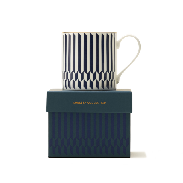 The Sloane Mug, a white luxury mug adorned with a navy blue and white chevron-stripe pattern, is elegantly presented on a matching teal gift box embossed with CHELSEA COLLECTION in gold lettering. Highlighting British craftsmanship, both the mug and the box display geometric vertical designs set against a crisp white backdrop.
