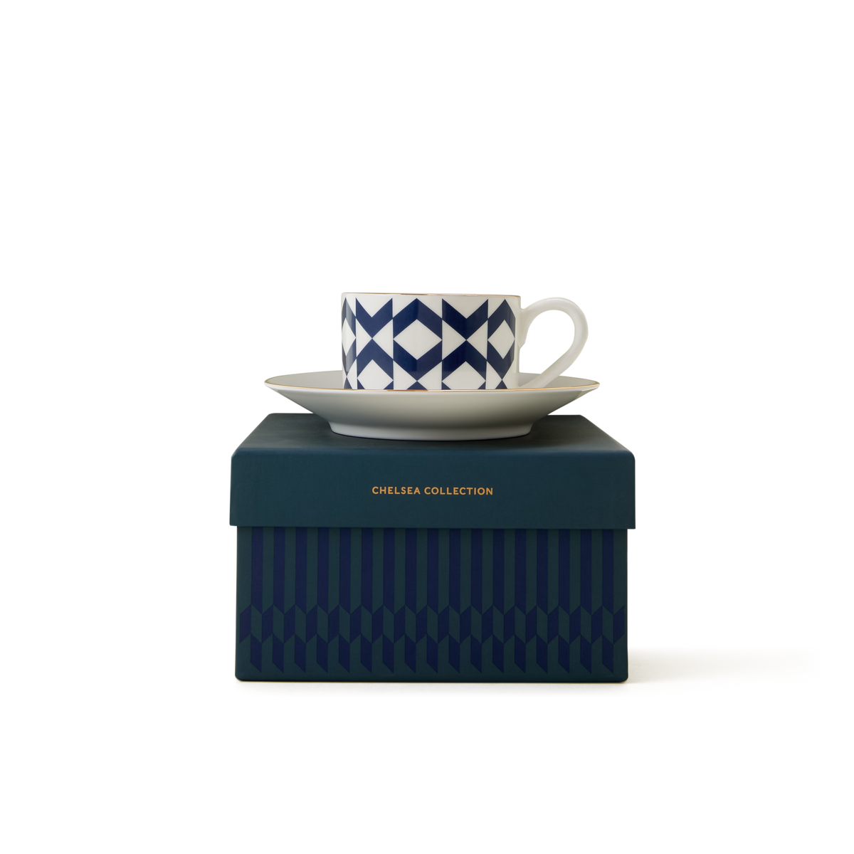 A white cup with a blue geometric pattern sits on a saucer, both placed on top of a dark blue box labeled Chelsea Collection in gold text. The background is plain white.