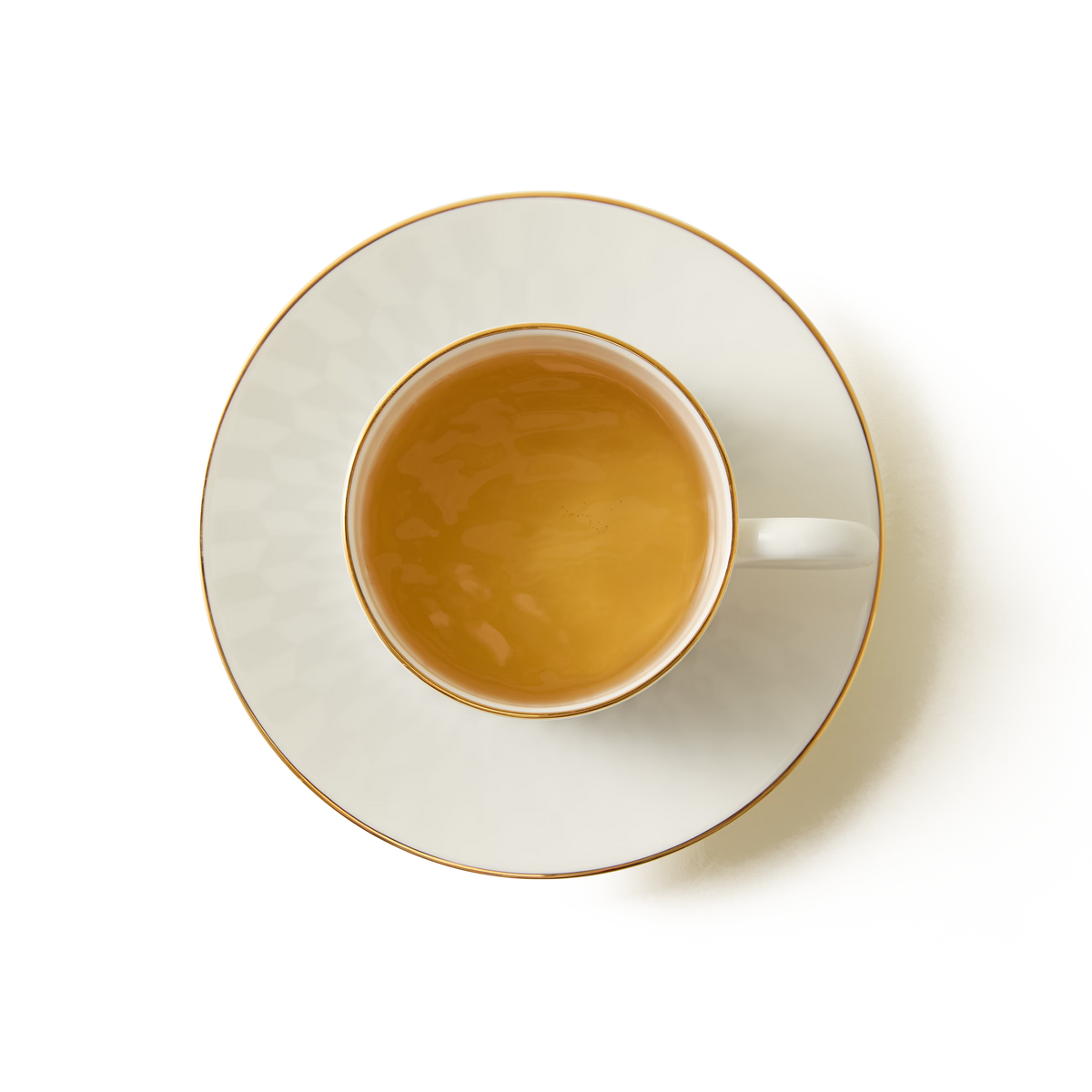 A white porcelain teacup filled with tea, placed on a matching saucer with a gold rim, viewed from above on a white background.