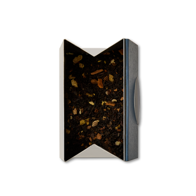 An open rectangular tin of Earl Grey Chai Loose Leaf Tea, viewed from above and filled with dark tea leaves blended with small pieces of spices or herbs.