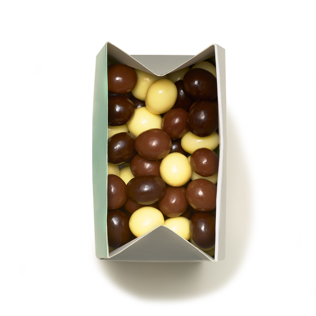 A rectangular box filled with Milk, Dark & White Chocolate Coated Espresso Beans in brown and yellow hues, viewed from above on a white background.