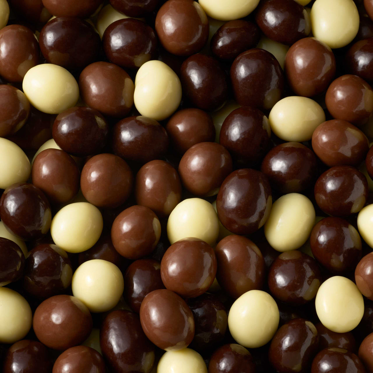 A close-up, high-angle shot shows a densely packed, chaotic pile of Milk, Dark & White Chocolate Coated Espresso Beans. The spheres have a smooth and glossy texture, featuring a variety of light cream hues alongside different shades of milk and dark chocolate, all nestled tightly together.
