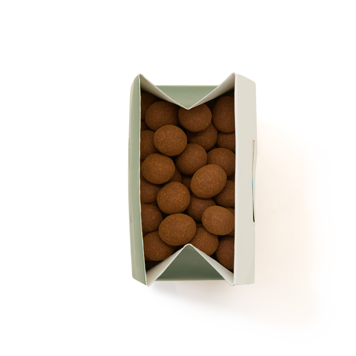 A top-down view of a partially opened white box filled with round, brown candies or tablets, arranged closely together against a plain white background.