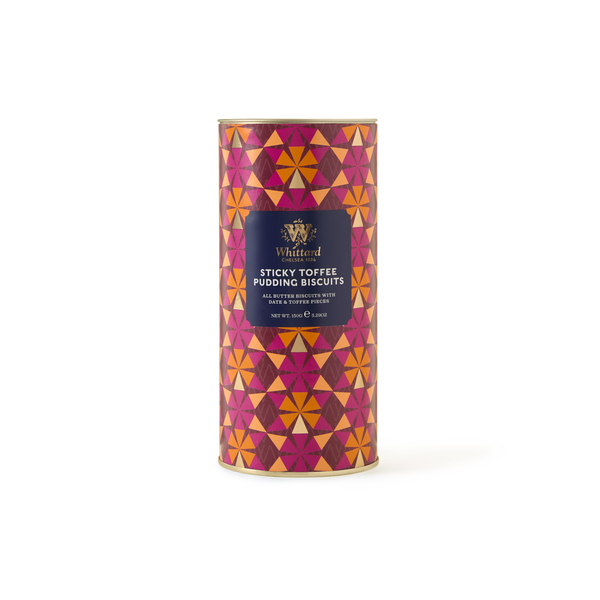 The Sticky Toffee Pudding Biscuits come in a cylindrical tin decorated with a bold geometric pattern in shades of red, orange, and pink, accented by a purple label on the front. These biscuits deliver the rich taste of classic puddings in every bite, making them an ideal gift for anyone who enjoys traditional British treats.