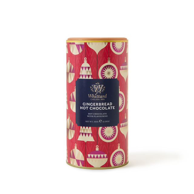 A red cylindrical tin of Whittard Gingerbread Hot Chocolate decorated with gold, white, and pink hanging ornaments on a festive background.
