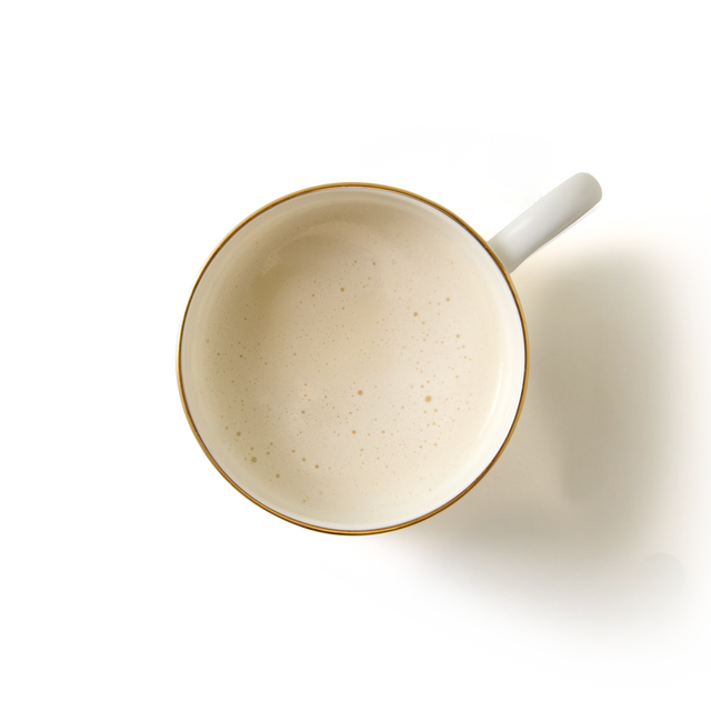 Overhead view of a white cup filled with frothy, creamy Toffee Apple White Hot Chocolate, casting a soft shadow on a plain white background.