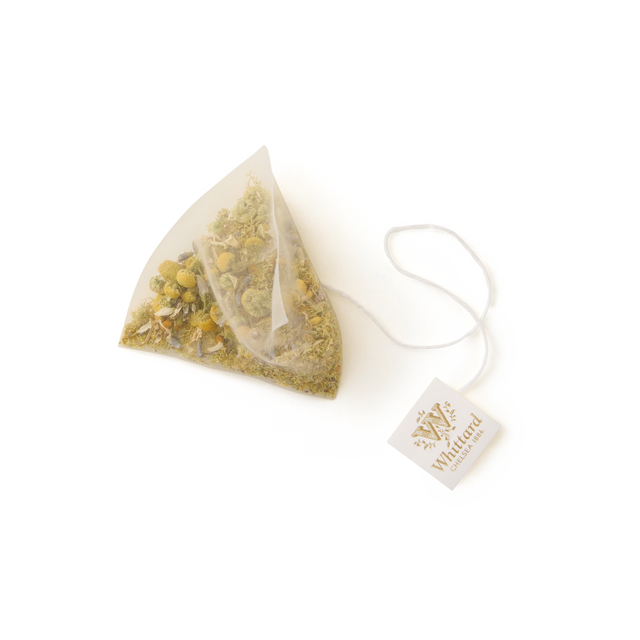 A single Camomile, Lavender and Bee Pollen Pyramid Teabag, filled with a soothing blend of loose botanicals for a calming caffeine-free tea, is attached to a string with a branded tag and displayed on a plain white background.