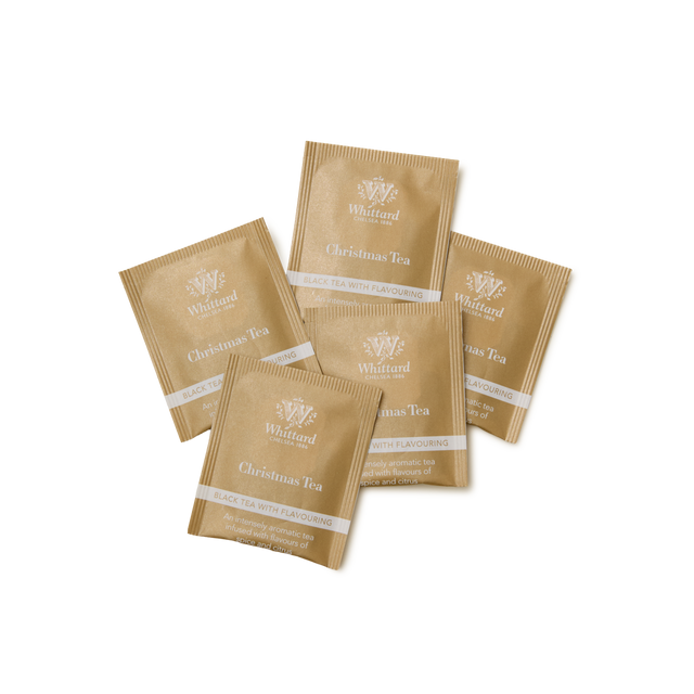 Five gold-colored sachets of Whittard Christmas Tea 25 Individually Wrapped Teabags arranged in a fan shape on a white background. Each sachet is labeled “Black tea with flavouring.”.