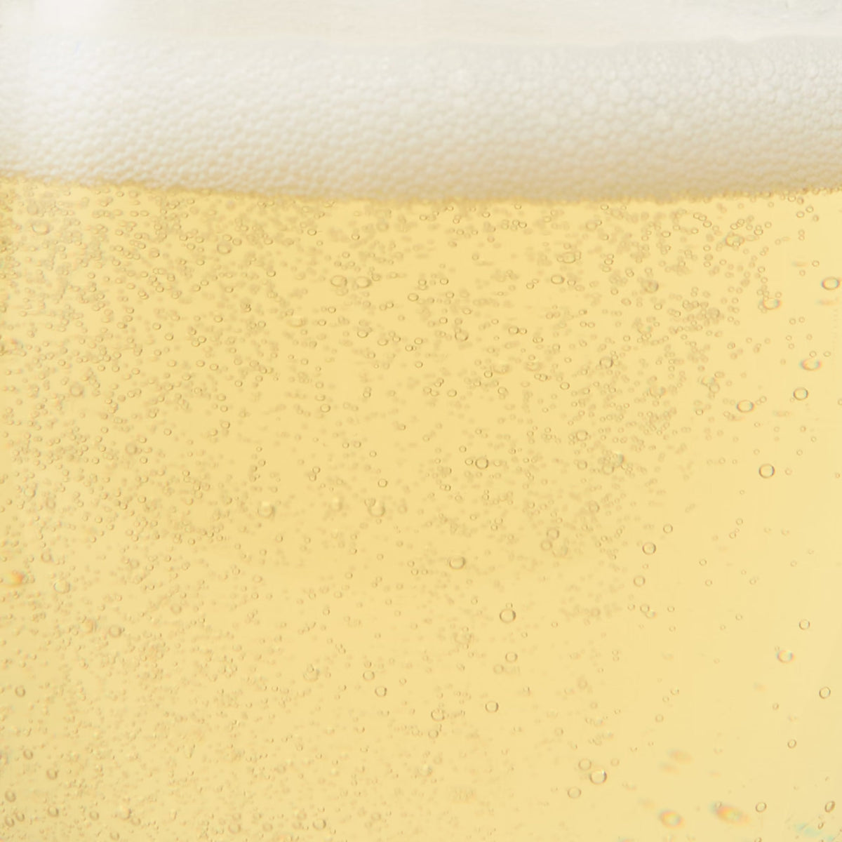 Close-up of a glass of Sparkling Green Tea Infusion showing golden liquid, rising bubbles, and a layer of white foam on top.