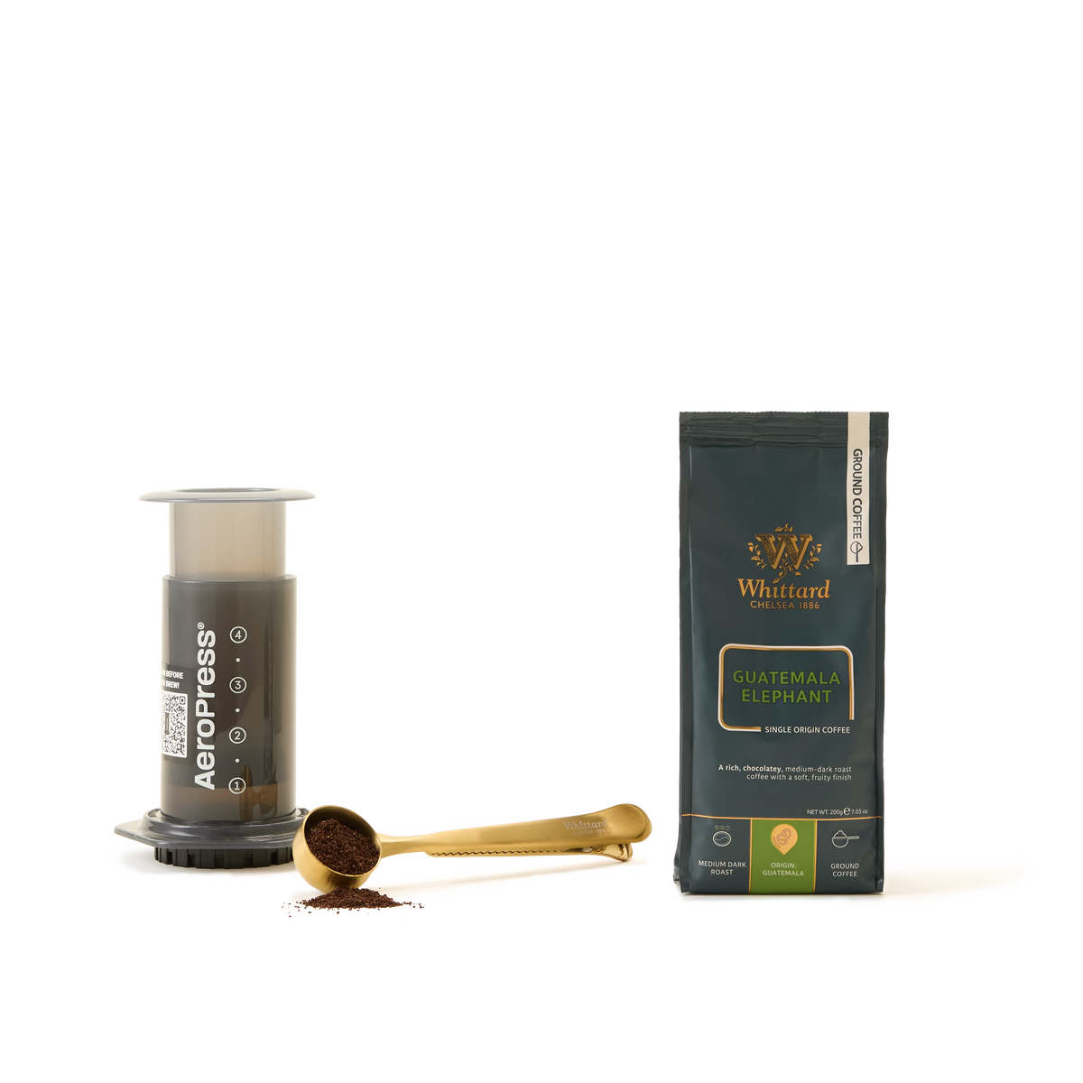 An AeroPress Coffee Starter Kit, a gold coffee scoop with ground coffee, and a bag of Whittard Guatemala Elephant ground coffee are arranged on a white background—perfect essentials for anyone passionate about exceptional coffee brewing.