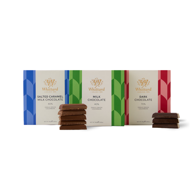The Chocolate Bar Trio features three Whittard bars—Salted Caramel Milk, Milk Chocolate, and Dark Chocolate—each displayed with a small stack of chocolate pieces in front of their vibrant packaging on a white background, all crafted with single origin Colombian cocoa for an exceptional taste experience.