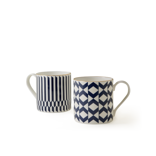 The Chelsea Collection Mug Duo features two white ceramic mugs with blue geometric patterns—one adorned with vertical stripes and hexagons, and the other displaying a repeating diamond and triangle design. Showcasing British craftsmanship, both mugs are equipped with handles and presented against a plain white background.