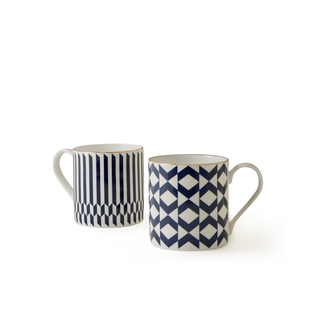 The Chelsea Collection Mug Duo features two white ceramic mugs with blue geometric patterns—one adorned with vertical stripes and hexagons, and the other displaying a repeating diamond and triangle design. Showcasing British craftsmanship, both mugs are equipped with handles and presented against a plain white background.