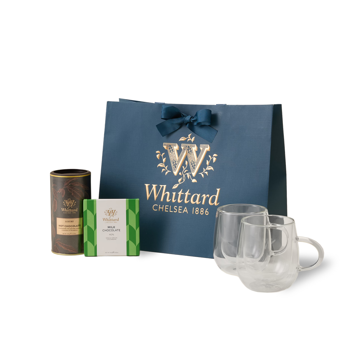 The Chocolate Indulgence Set features a blue Whittard gift bag with gold lettering, a tin of luxury hot chocolate, a box of chocolates, and two clear glass mugs—all beautifully arranged on a white background—making this the perfect chocolate gift set for any occasion.
