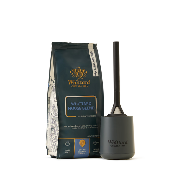 A Coffee Lovers Kit featuring Whittard House Blend ground coffee stands next to a dark, handled container—both labeled Whittard. The set showcases the House Blend’s dark colors, gold accents, and blend details that emphasize its status as a speciality coffee. The background is white.