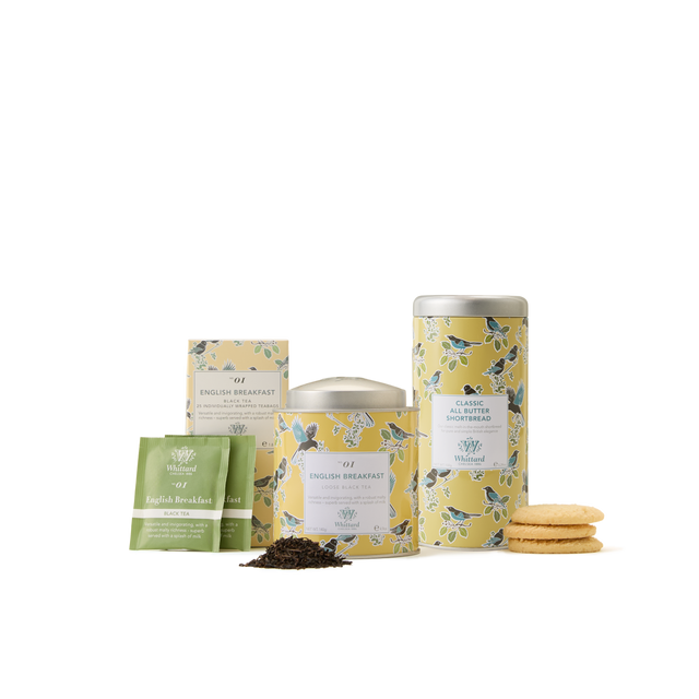A delightful British tea gift, The English Breakfast Collection includes two tins, tea bags, a small pack, loose leaf English Breakfast tea, and a stack of cookies—each elegantly wrapped in yellow floral packaging on a white background.