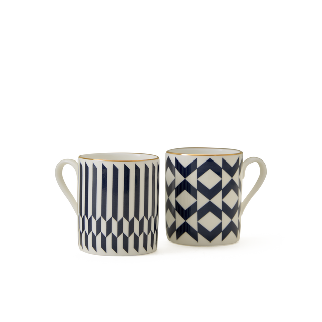 The Chelsea Collection Espresso Cup Duo features two ceramic mugs with handles, each showcasing modern geometric patterns in navy blue and white that exemplify exceptional British craftsmanship. The mug on the left displays striking vertical stripes and cube motifs, while the mug on the right is adorned with an elegant diamond and chevron design. Both pieces are finished with exquisite 22ct gold detailing, bringing a luxurious touch to your drinkware collection.