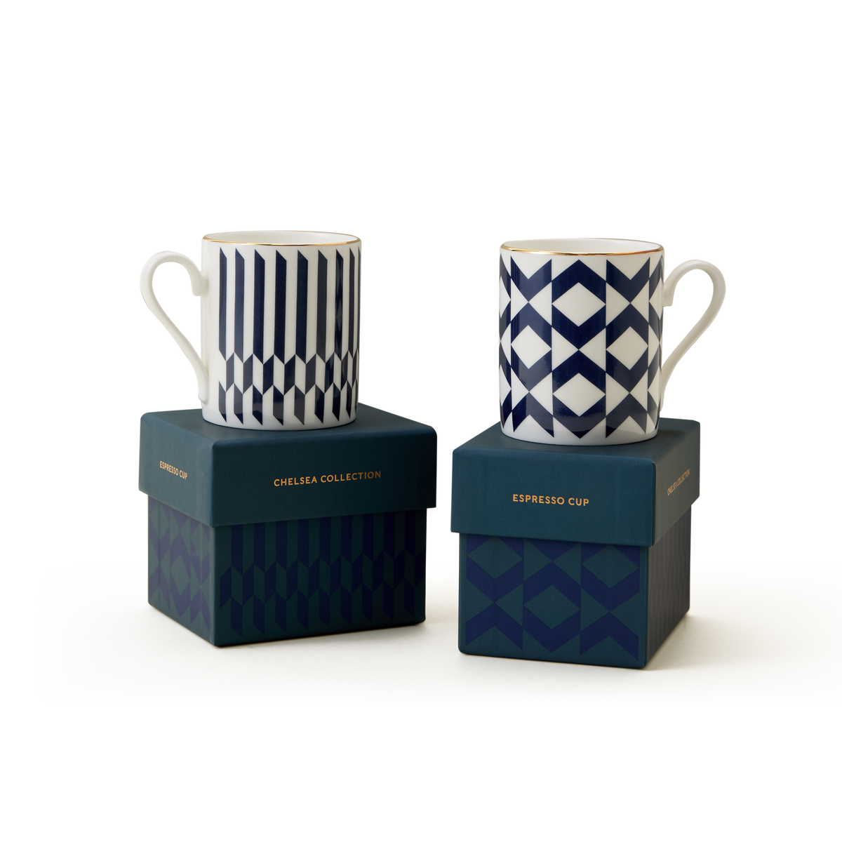 Two white espresso cups with blue geometric patterns sit atop blue boxes labeled “The Chelsea Collection Espresso Cup Duo.” Showcasing exquisite British craftsmanship, the boxes also feature dark blue geometric designs, all set against a plain white background.