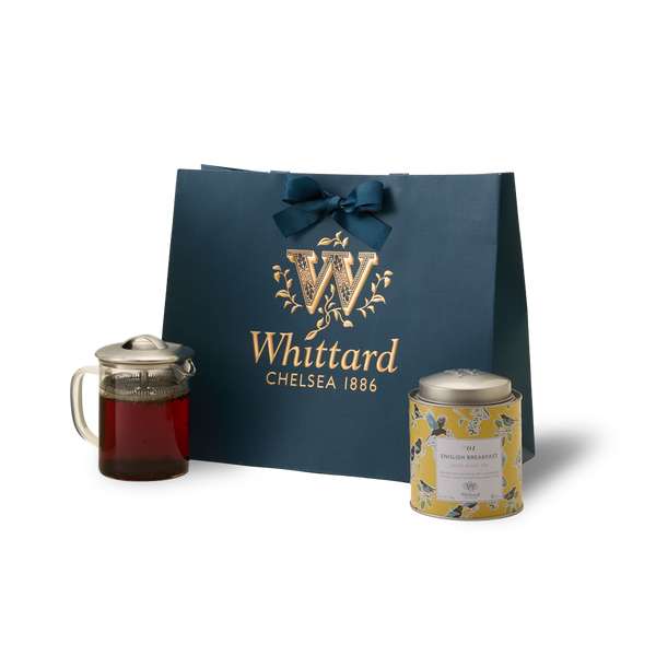 The Greenwich Tea Collection features a blue Whittard gift bag tied with a bow, a Greenwich Teapot filled with brewed loose leaf tea, and a decorative tin of English Breakfast tea, artfully arranged on a white background—perfect as a personalised tea gift.