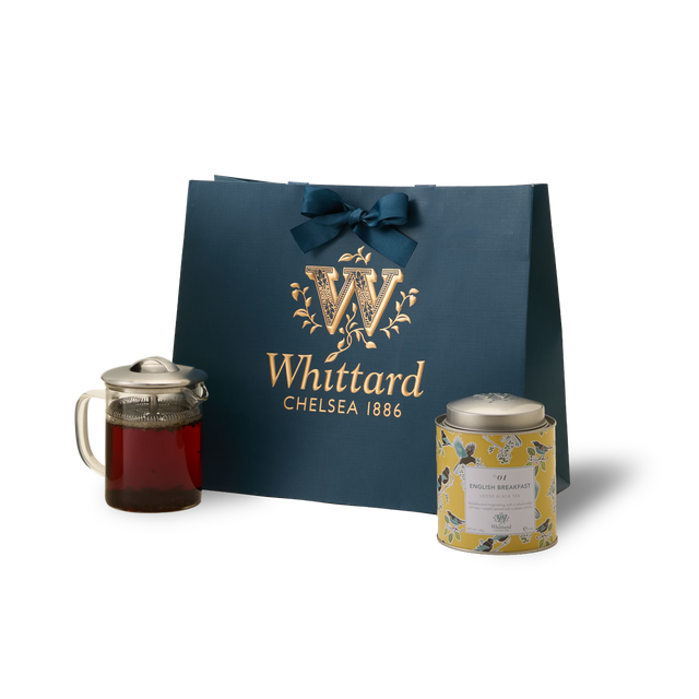 The Greenwich Tea Collection features a blue Whittard gift bag tied with a bow, a Greenwich Teapot filled with brewed loose leaf tea, and a decorative tin of English Breakfast tea, artfully arranged on a white background—perfect as a personalised tea gift.