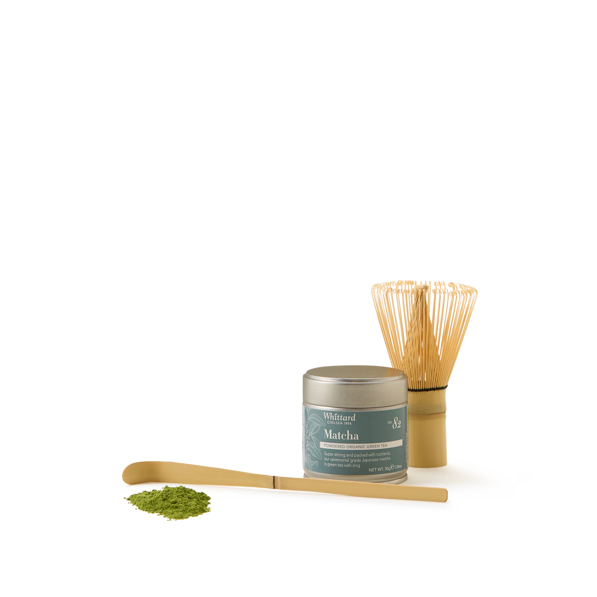 The Matcha Must-Have Collection, featuring a tin of ceremonial grade matcha powder, a bamboo whisk, a bamboo scoop, and a small pile of matcha powder, is elegantly arranged on a plain white background.