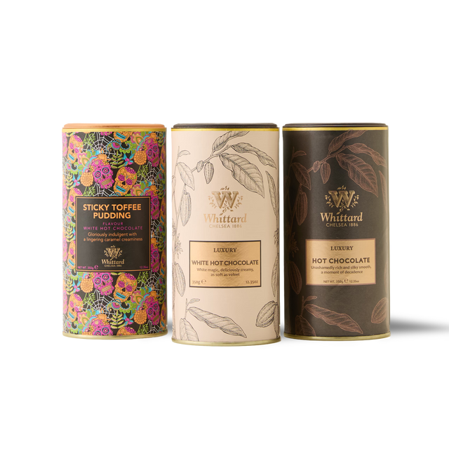 The trio of cylindrical tins from Whittard—Signature Hot Chocolate Trio—features a colorful floral Sticky Toffee Pudding Hot Chocolate, a cream-toned Luxury White Hot Chocolate, and a brown Luxury Hot Chocolate, all displayed side by side on a white background.